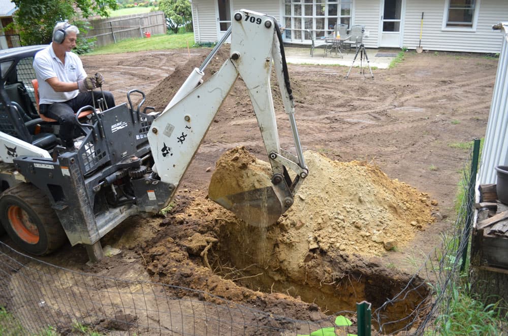 Trench excavation for a French drain with compact backhoe equipment